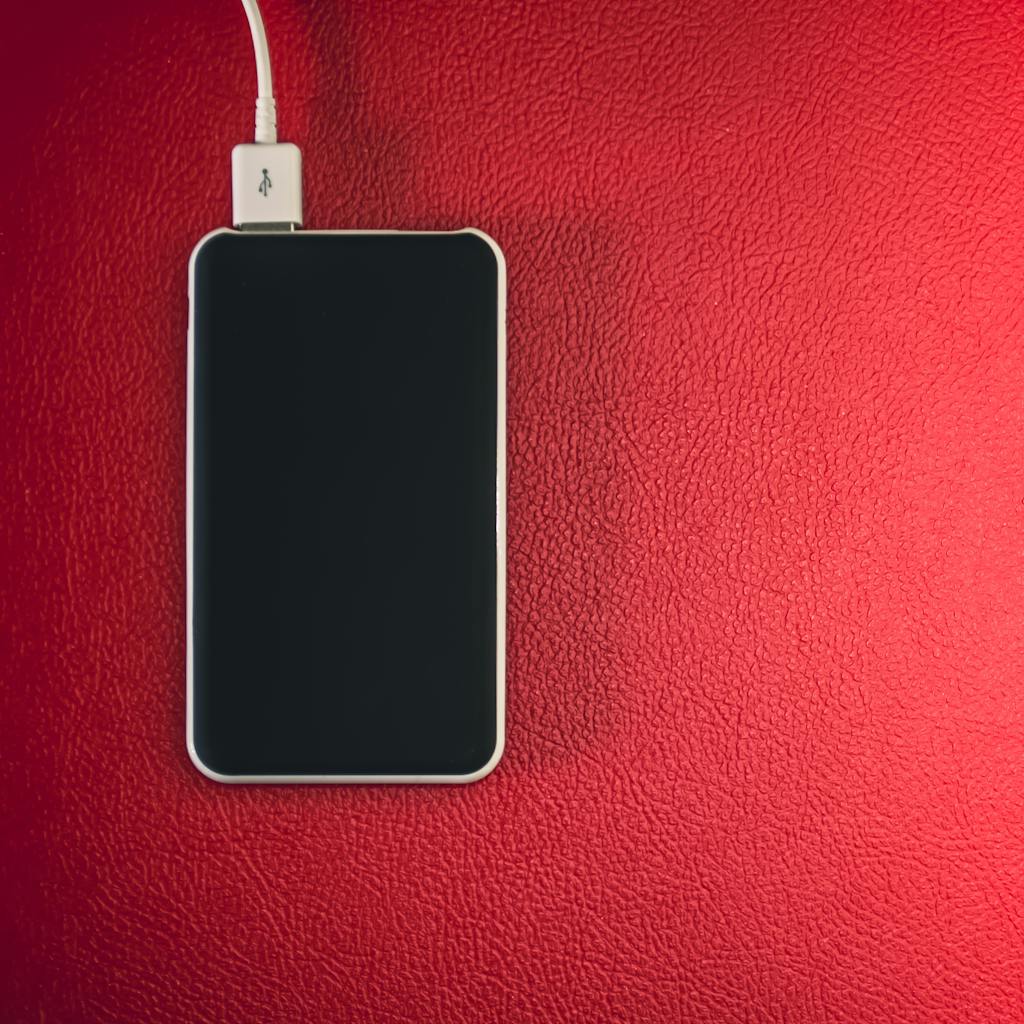A smartphone connected to a charger placed on a red leather surface.